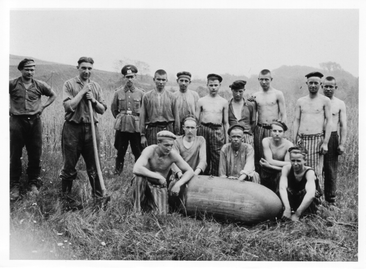 Häftlinge des Bombenräumkommandos „Kalkum“ mit einer entschärften Bombe, 1943/44. Bei dem Uniformierten handelt es sich vermutlich um einen Feuerwerker.