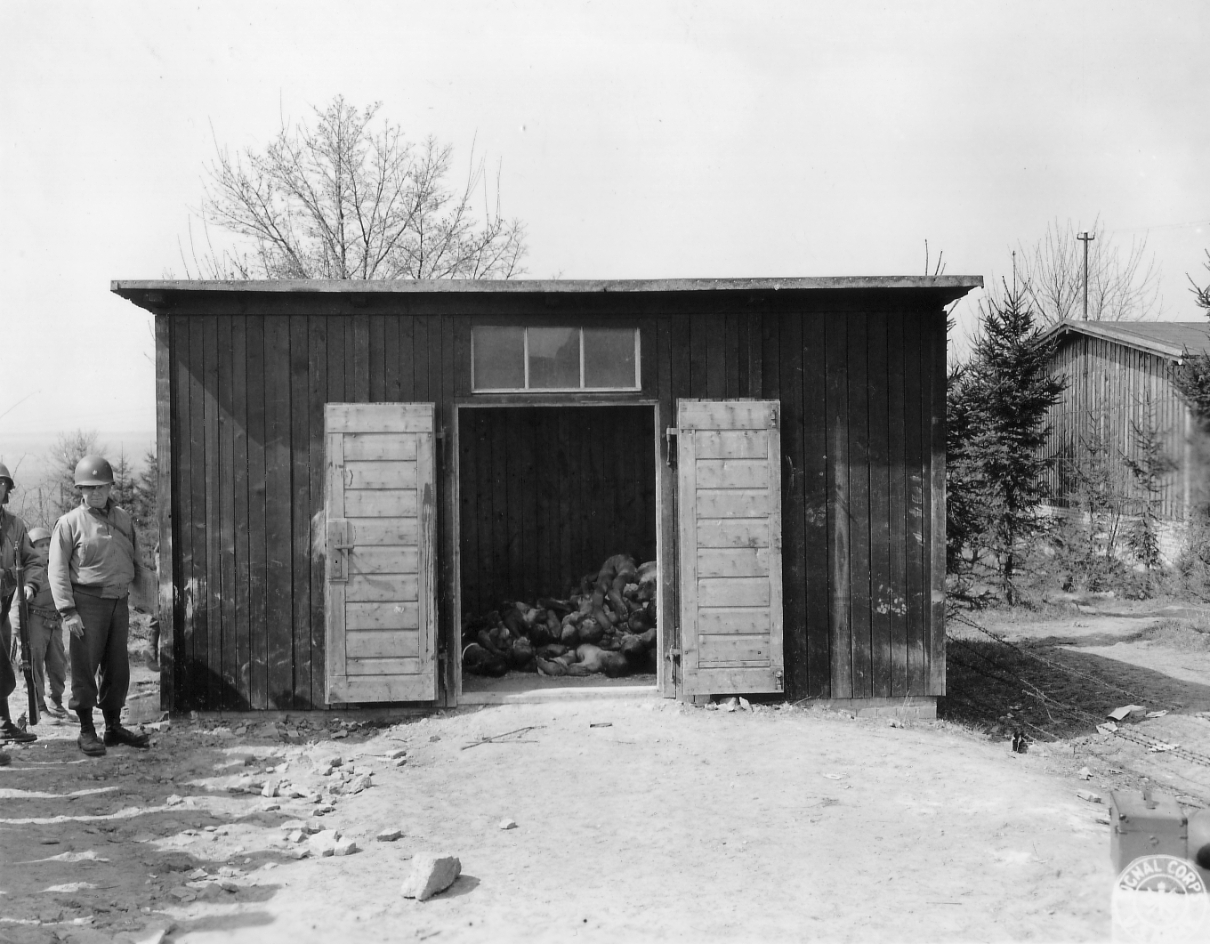 Soldaten der U.S. Army neben einer Baracke mit aufgestapelten Leichen im Nordlager, 10. April 1945