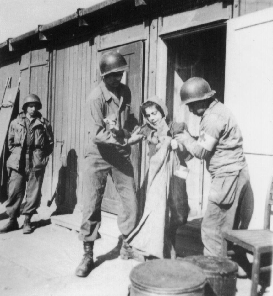 Zwei Sanitäter stützen eine Überlebende auf ihrem Weg aus einer Baracke zum Krankenwagen, 17. April 1945. Foto: David E. Scherman