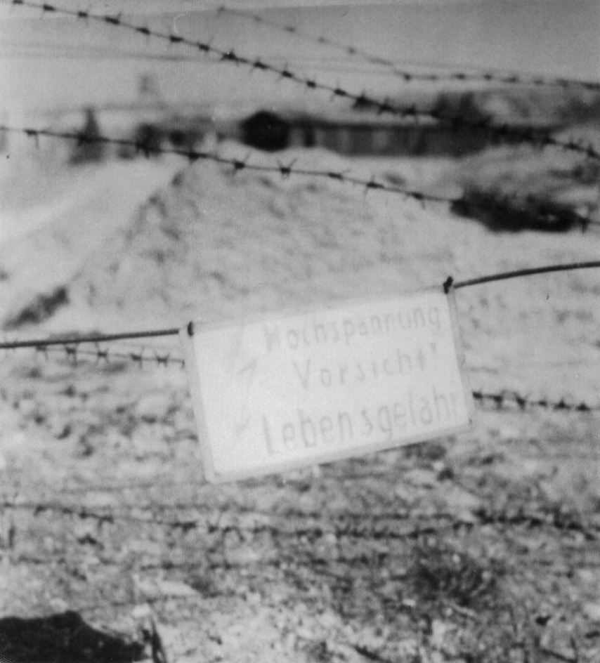 Schild am Lagerzaun mit der Aufschrift: „Hochspannung. Vorsicht Lebensgefahr“, 17. April 1945. Foto: David E. Scherman