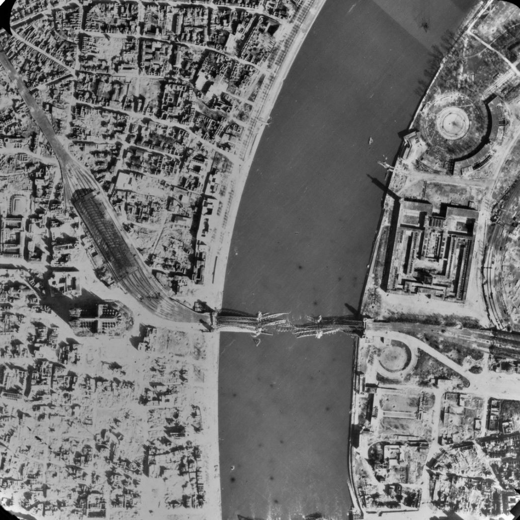 Blick auf die linksrheinische Innenstadt von Köln um den Hauptbahnhof, den Dom und die zerstörte Hohenzollernbrücke. Auf der rechten Rheinseite ist das Kölner Messegelände zu sehen, wo die Häftlinge untergebracht waren. Aufnahme der alliierten Luftaufklärung, 11. April 1945.