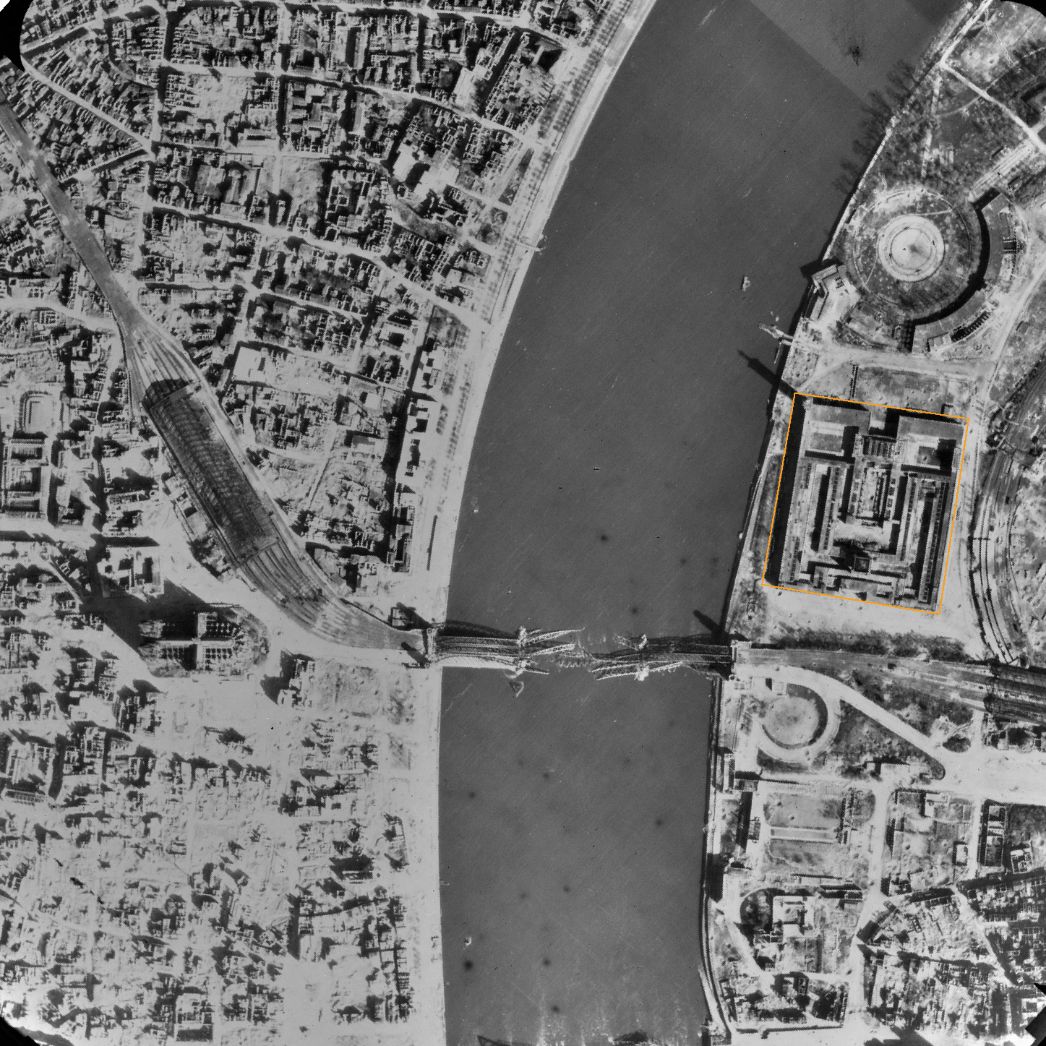 Blick auf die linksrheinische Innenstadt von Köln um den Hauptbahnhof, den Dom und die zerstörte Hohenzollernbrücke. Auf der rechten Rheinseite ist das Kölner Messegelände (markiert) zu sehen, wo die Häftlinge untergebracht waren. Aufnahme der alliierten Luftaufklärung, 11. April 1945.