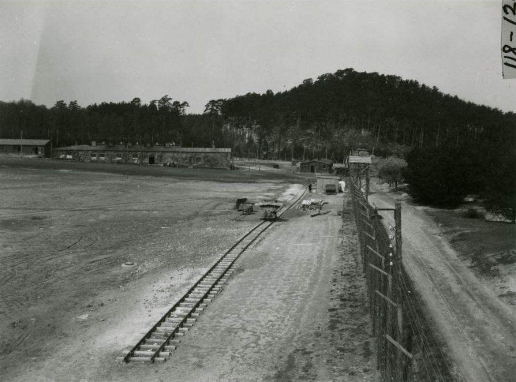 Ein Teil des Appellplatzes und des Lagerzauns mit Wachturm und den Gleisen einer Lorenbahn, Mitte April 1945. Foto: Preston A. Reed (U.S. Army Signal Corps)
