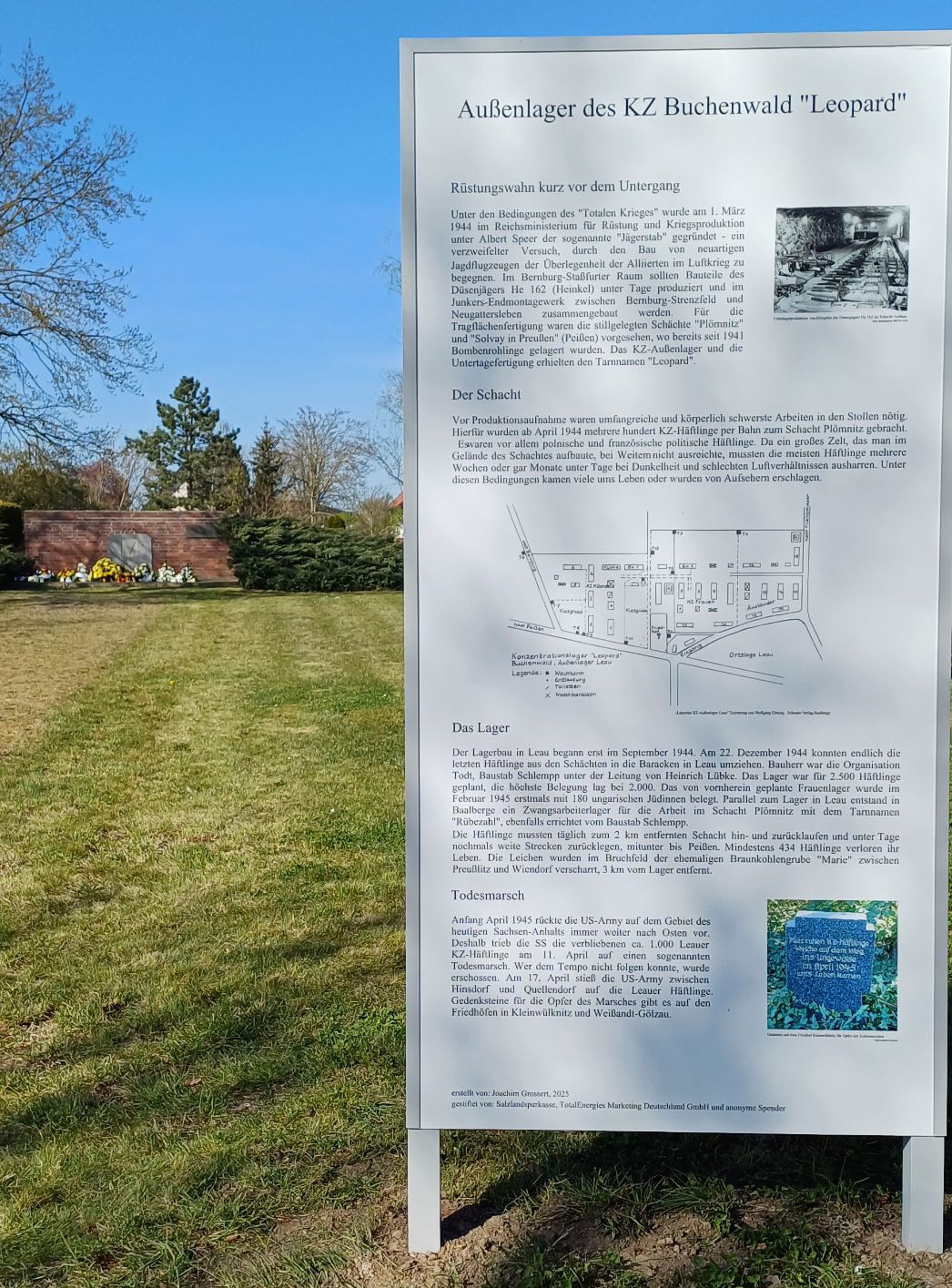 Informationstafel auf dem Friedhof in Leau mit dem Gedenkstein im Hintergrund, 2025. Foto: Kerstin Schmidt