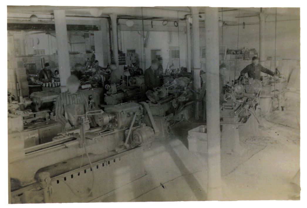 KZ-Häftlinge in gestreifter Kleidung und vermutlich deutsche und ausländische Arbeiter in einer der Produktionshallen der HEMAF in Osterode, 1944/45