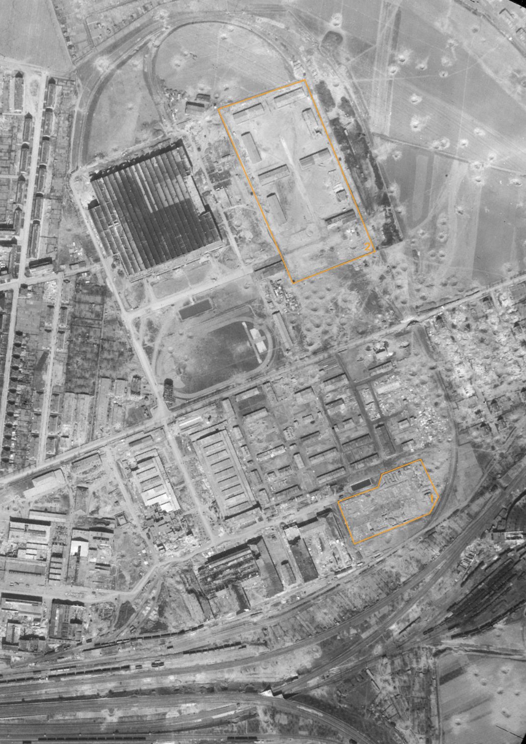Das weitgehend zerstörte Areal des Fritz-Sauckel-Werks in Weimar. Aufnahme der alliierten Luftaufklärung, 10. April 1945 (Ausschnitt). Markiert sind das Gelände des ersten Barackenlagers, das im Februar 1945 zerstört wurde (1), sowie das im Herbst 1944 errichtete zweite Barackenlager (2) direkt neben der großen Werkzeugmaschinenfabrik des Fritz-Sauckel-Werks.