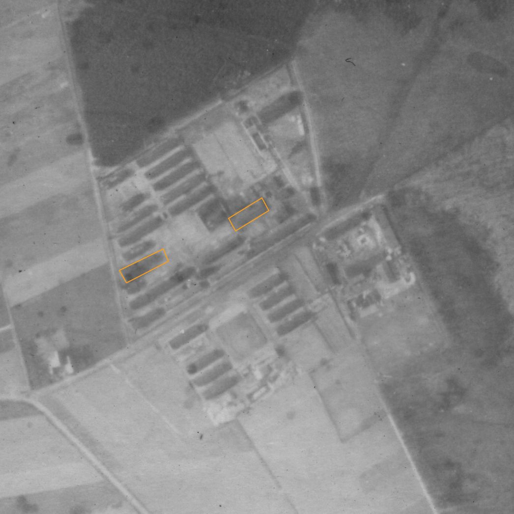 Das seit August 1940 bestehende ehemalige Häftlingslager mit angrenzendem Industriehof. Markiert sind die Unterkunftsbaracke (Block 4a, rechts) und die Häftlingsküche (links). Das Lager war rund einen Kilometer von der Wewelsburg entfernt. Unterhalb der Landstraße befand sich der ehemalige SS-Bereich mit Bauhof. Aufnahme der alliierten Luftaufklärung, 30. März 1945 (Ausschnitt)